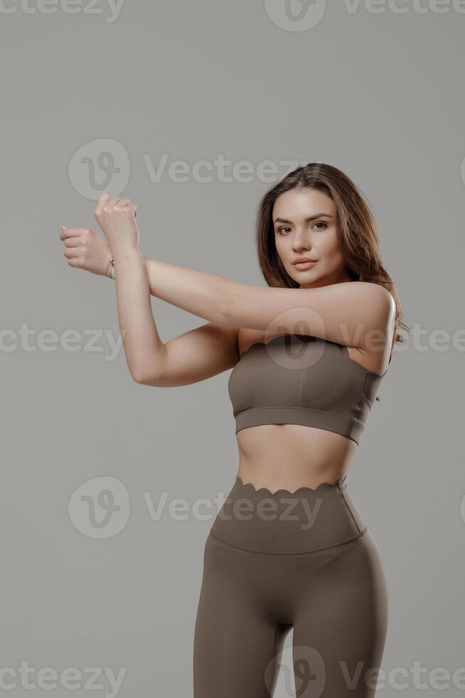 Woman stretching in workout attire against a simple gray background while preparing for fitness activities photo