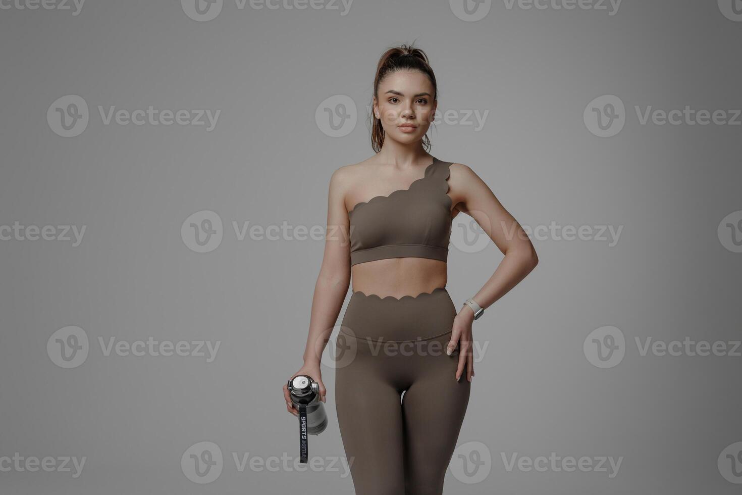 Fitness enthusiast in stylish activewear poses confidently with water bottle in a minimalistic studio setting during a workout session photo