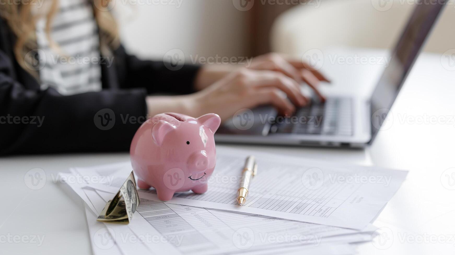 Managing personal finances with a laptop, piggy bank, and documents at a desk during daylight hours photo