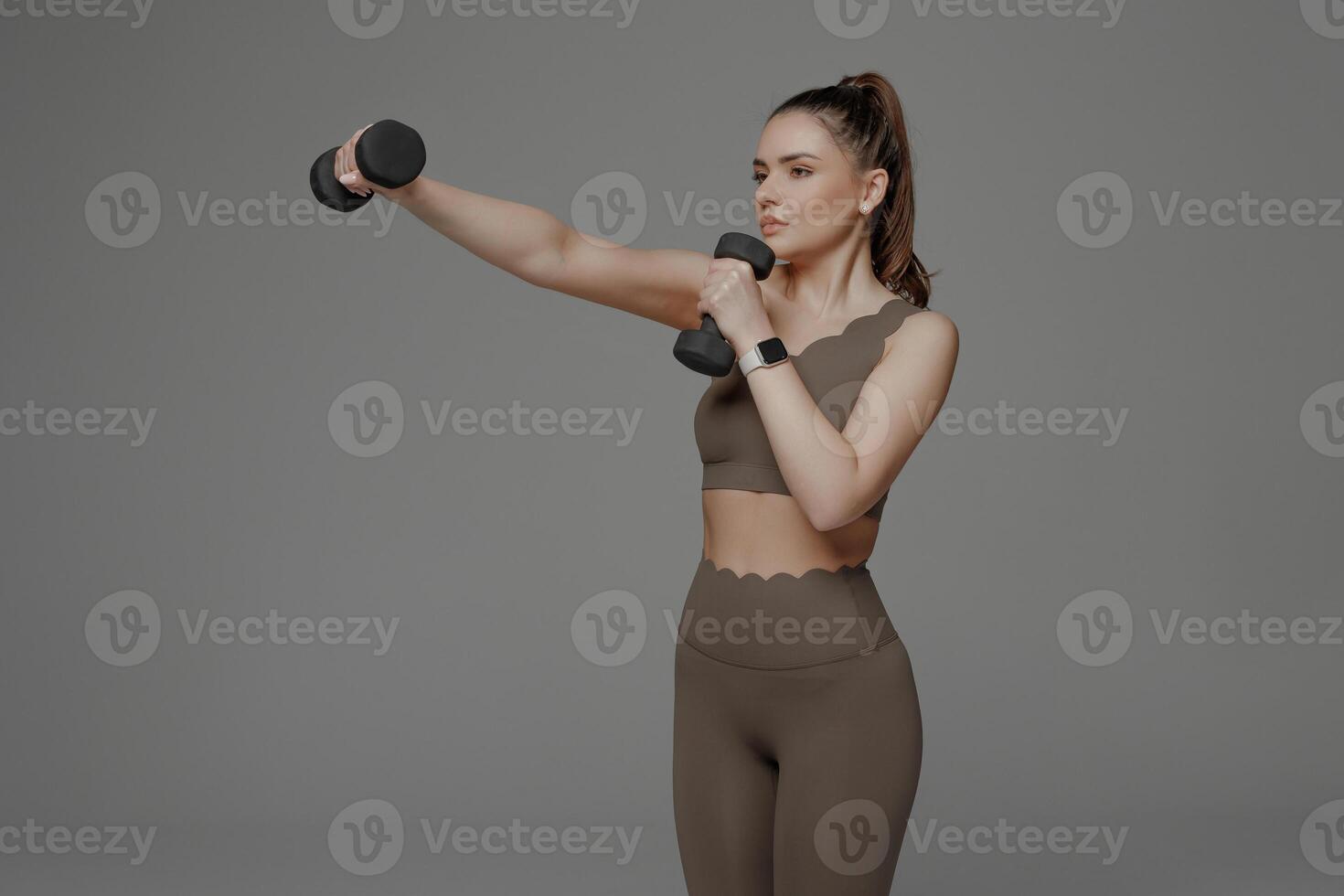 Fit woman exercising with dumbbells in a minimalist studio during morning workout session for strength training photo
