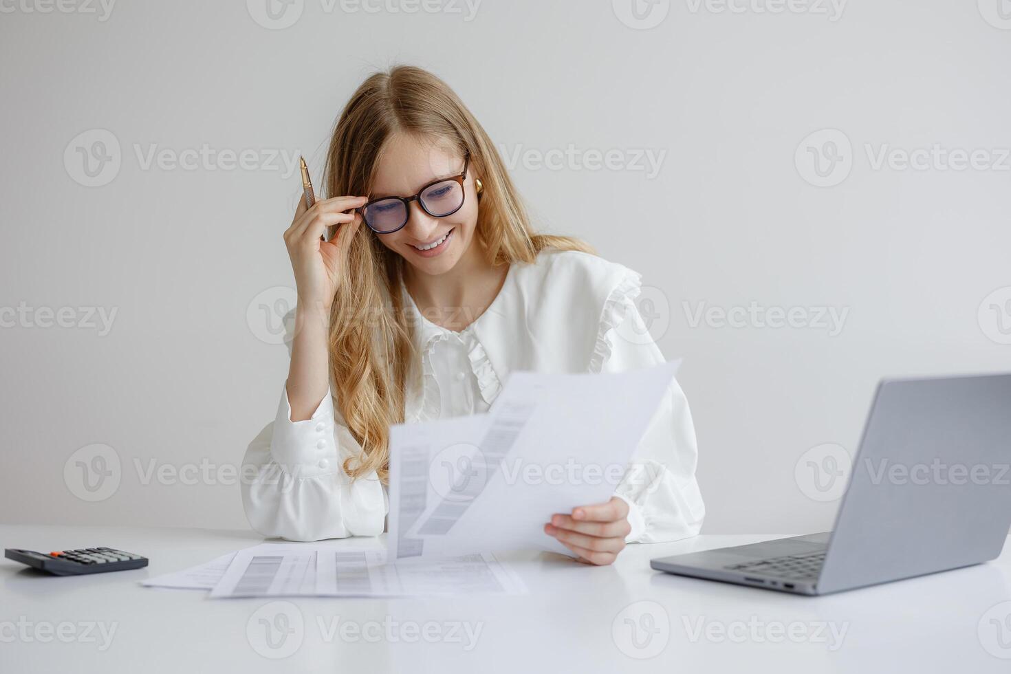 Young woman reviews financial documents while working at a desk with a laptop in a modern workspace photo