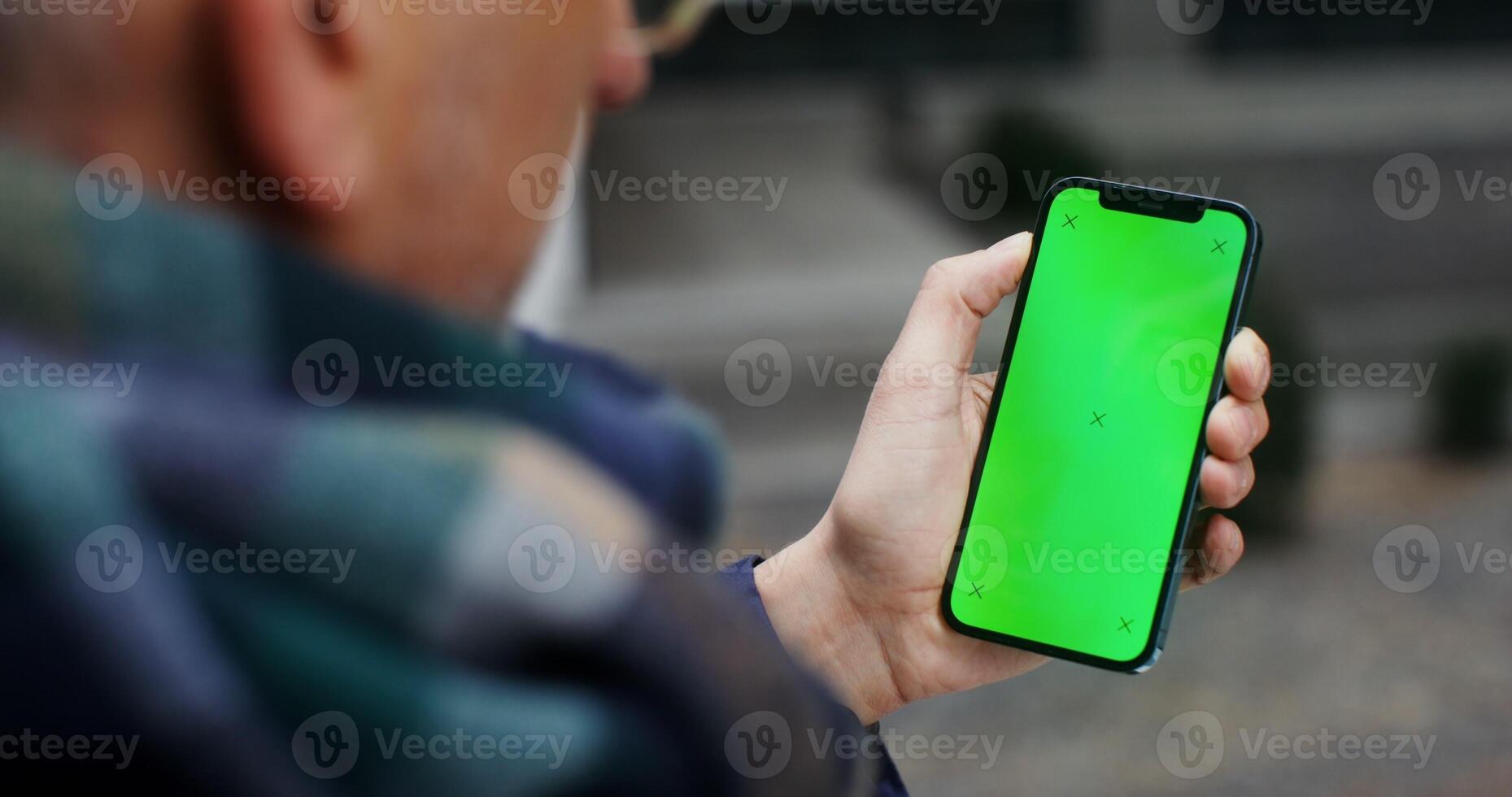 Gray-haired man using mobile phone with green screen swiping his finger across the screen to the side, unrecognizable person photo