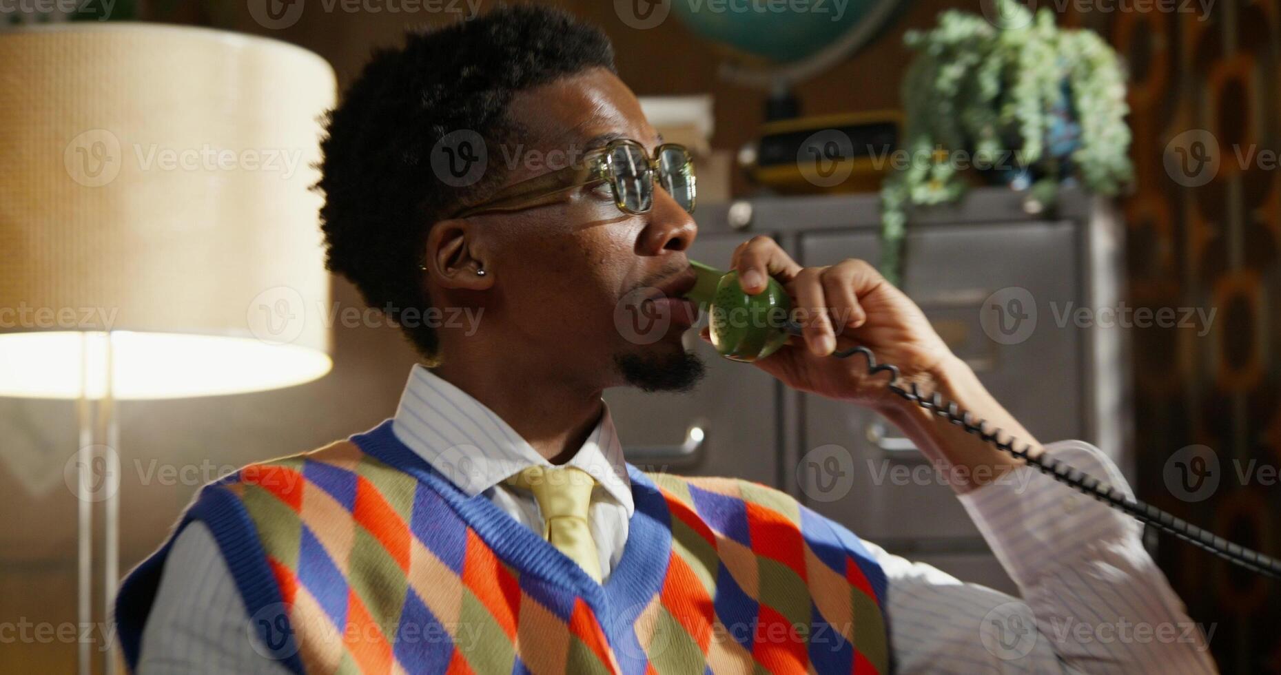 A man is smiling while talking on an analog phone. He's sitting in a retro room photo