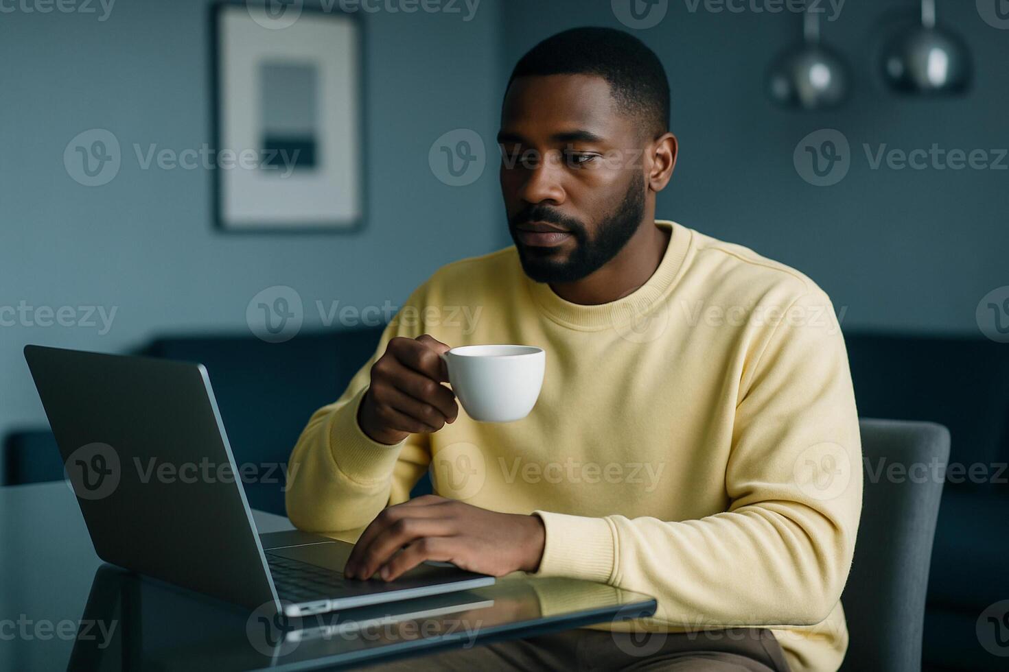 Black man drinking coffee while working on laptop at home, casual remote work setup, technology and modern lifestyle in home office photo