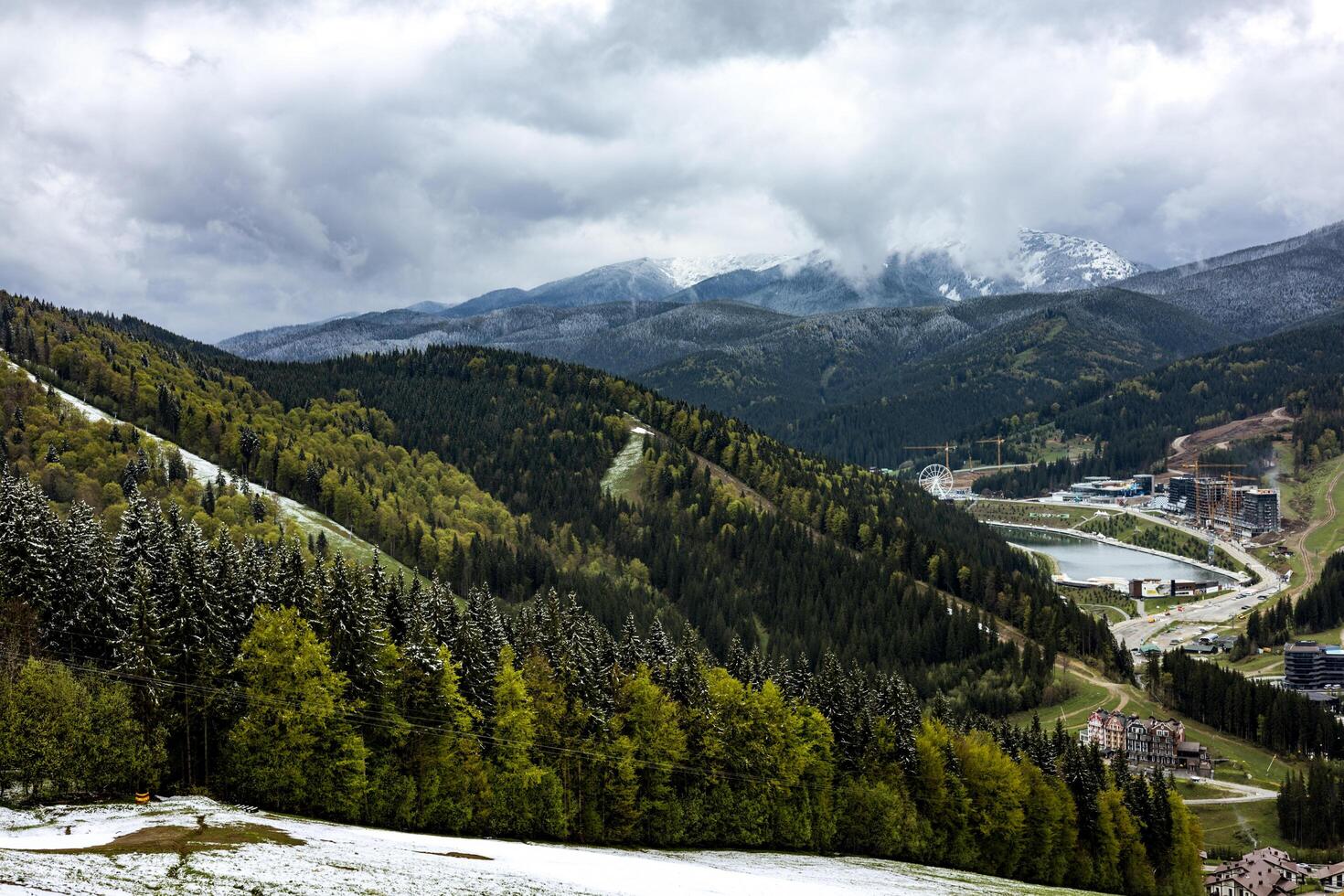 Stunning mountain landscape showcases a forest, lake, snowy peaks under a cloudy sky. A scenic view captures the breathtaking panorama of mountains, lush green forests, and a serene lake under skies photo