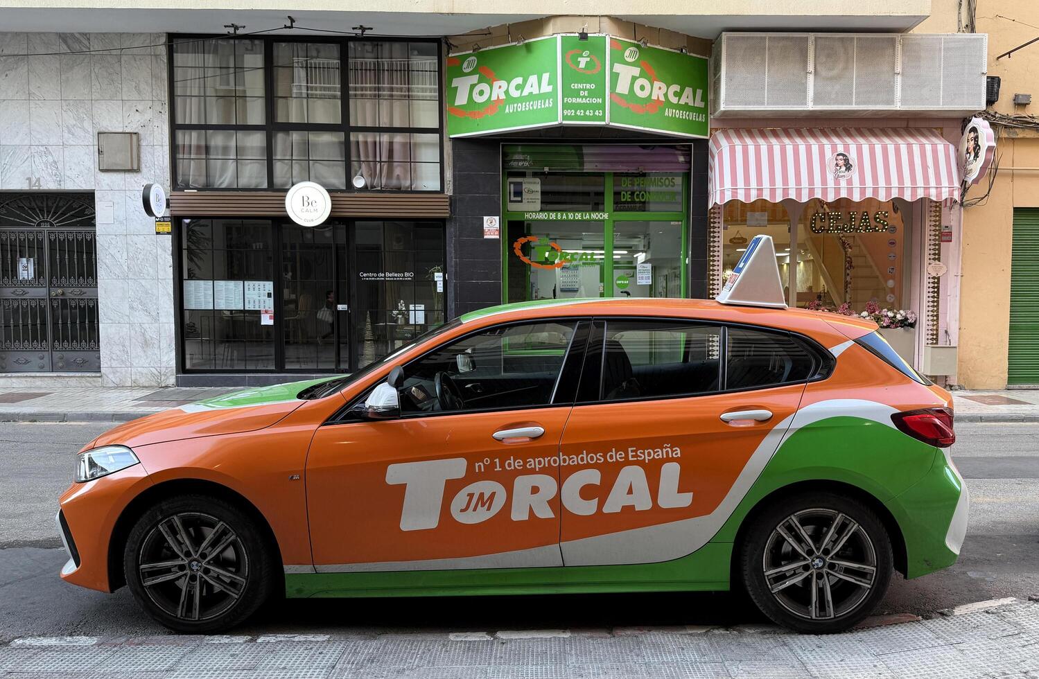 Malaga, Spain, May 18, 2025. Brightly colored car of driving school Torcal branding parked on a city street, promoting local business and services in urban environment photo
