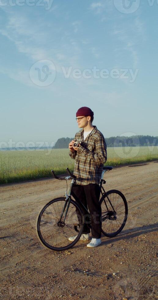 A young stylishly dressed man takes photographs with a camera while standing near a picturesque wheat field photo