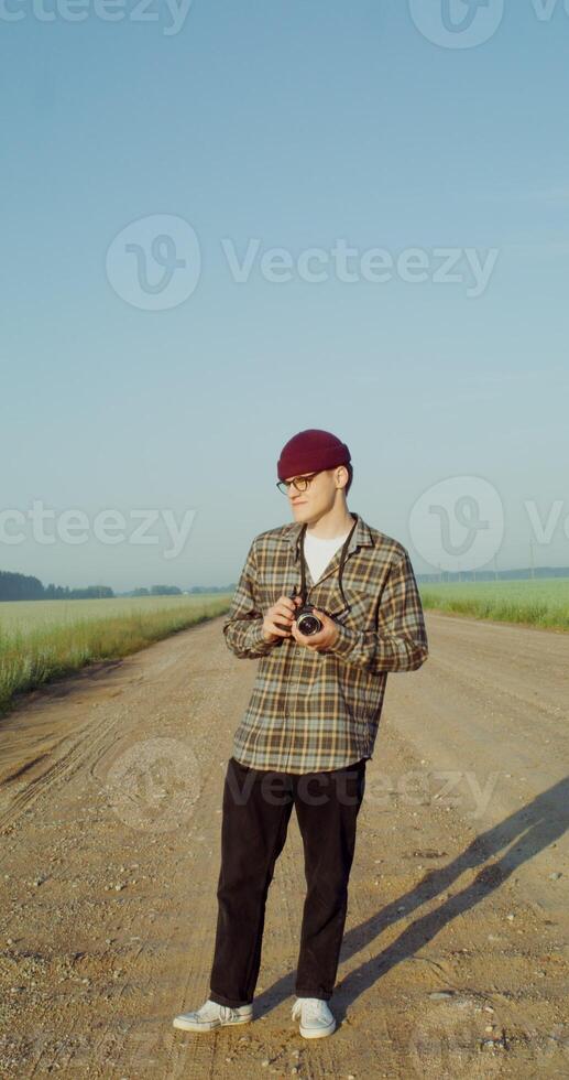 Male photographer takes photos while walking along a gravel road among agricultural fields on a sunny day. 4k vertical , red komodo
