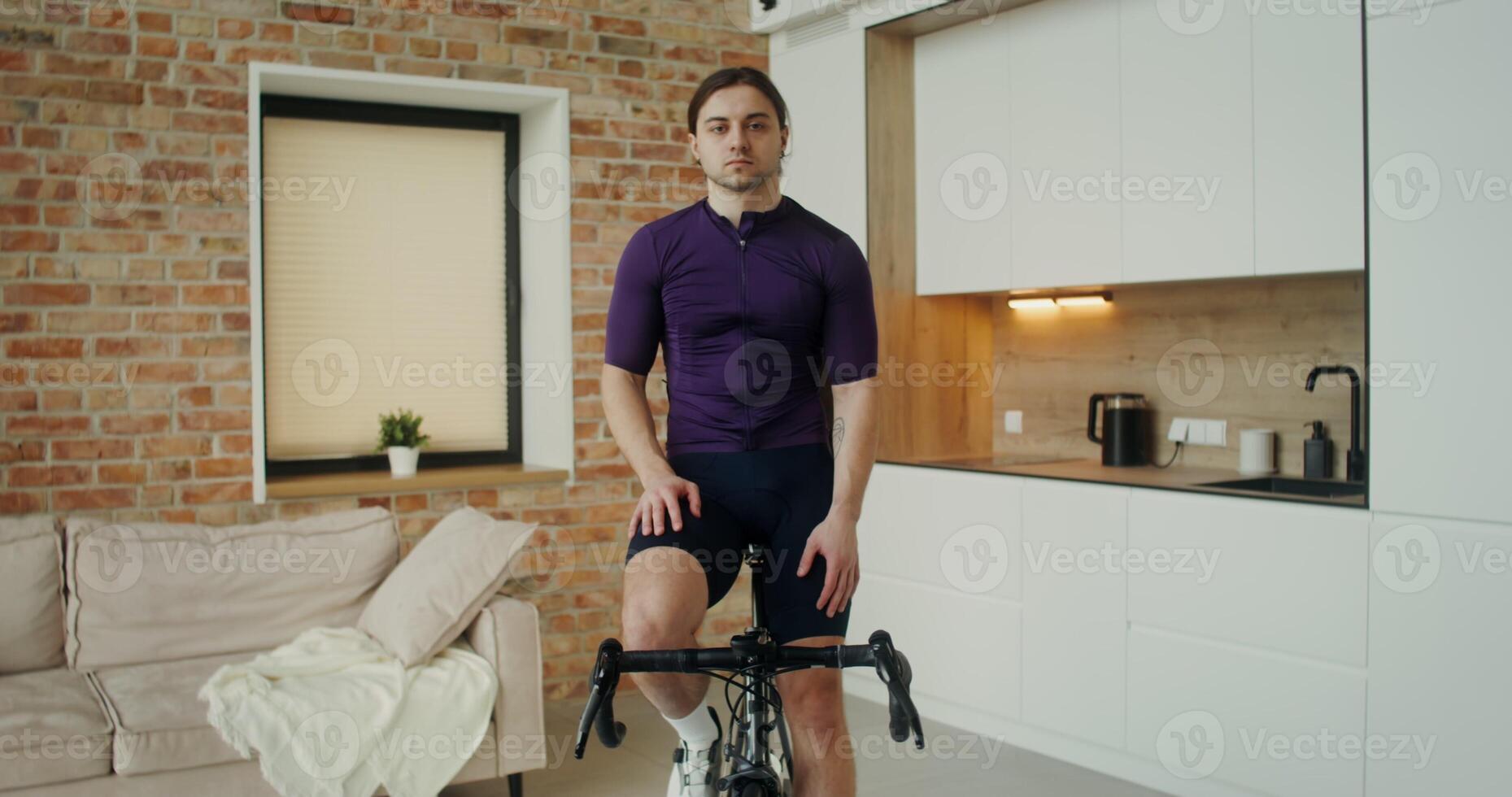 Man of European appearance of an athletic build looks at the camera while sitting on an exercise bike in a stylish home interior photo