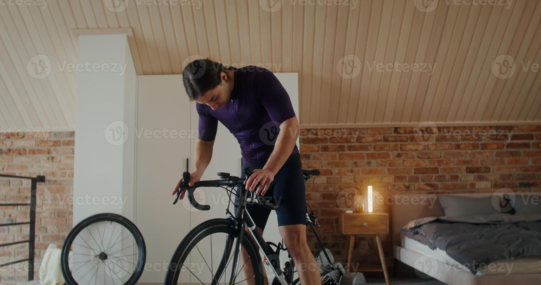 A man starts a bike workout at home bike station in a modern bedroom. Indoor cardio exercise bike photo