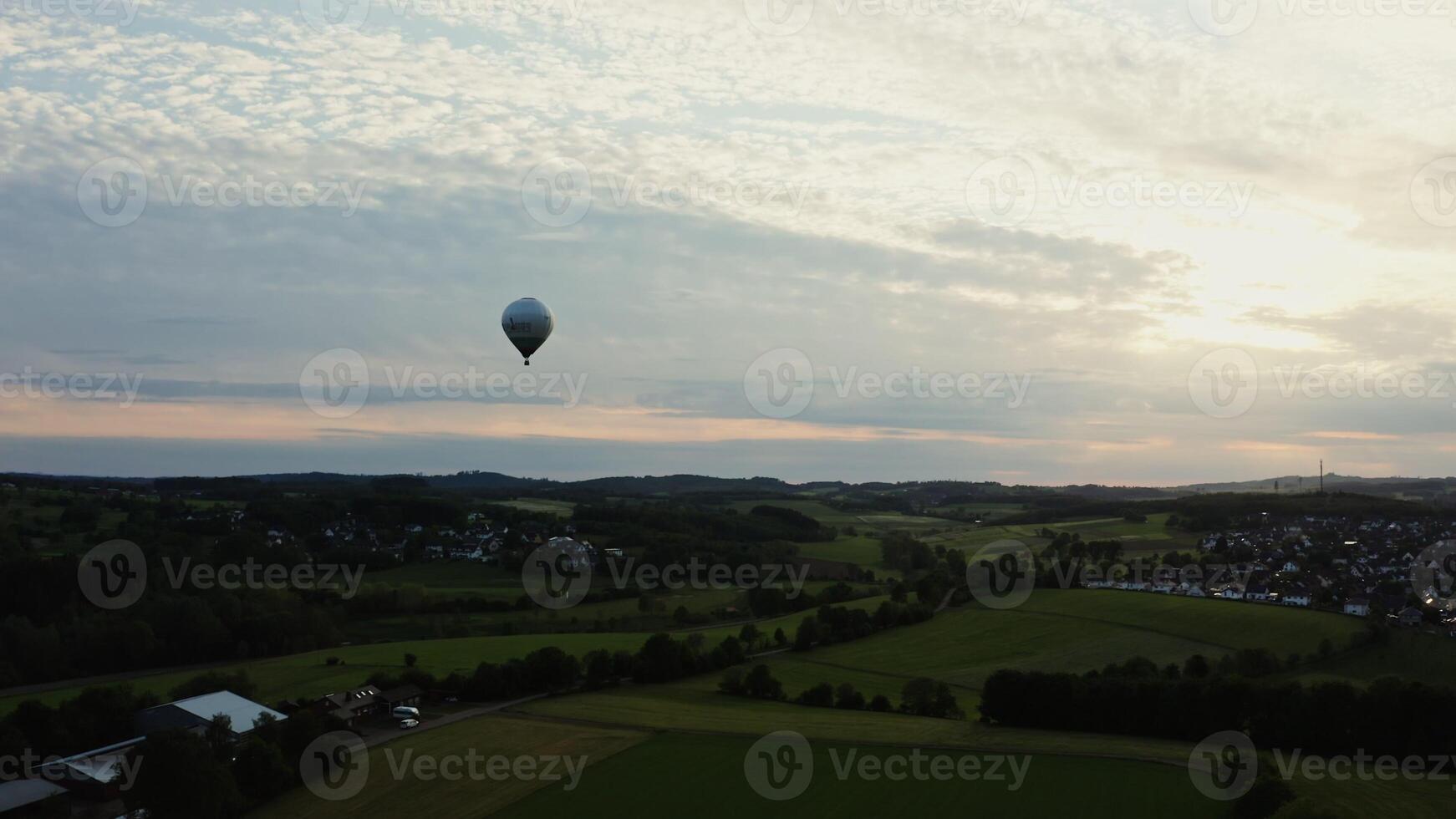 Shot of a hot air balloon in the sky flying over neat village houses nestled in a green forest. Aero shooting in the evening, Germany. photo
