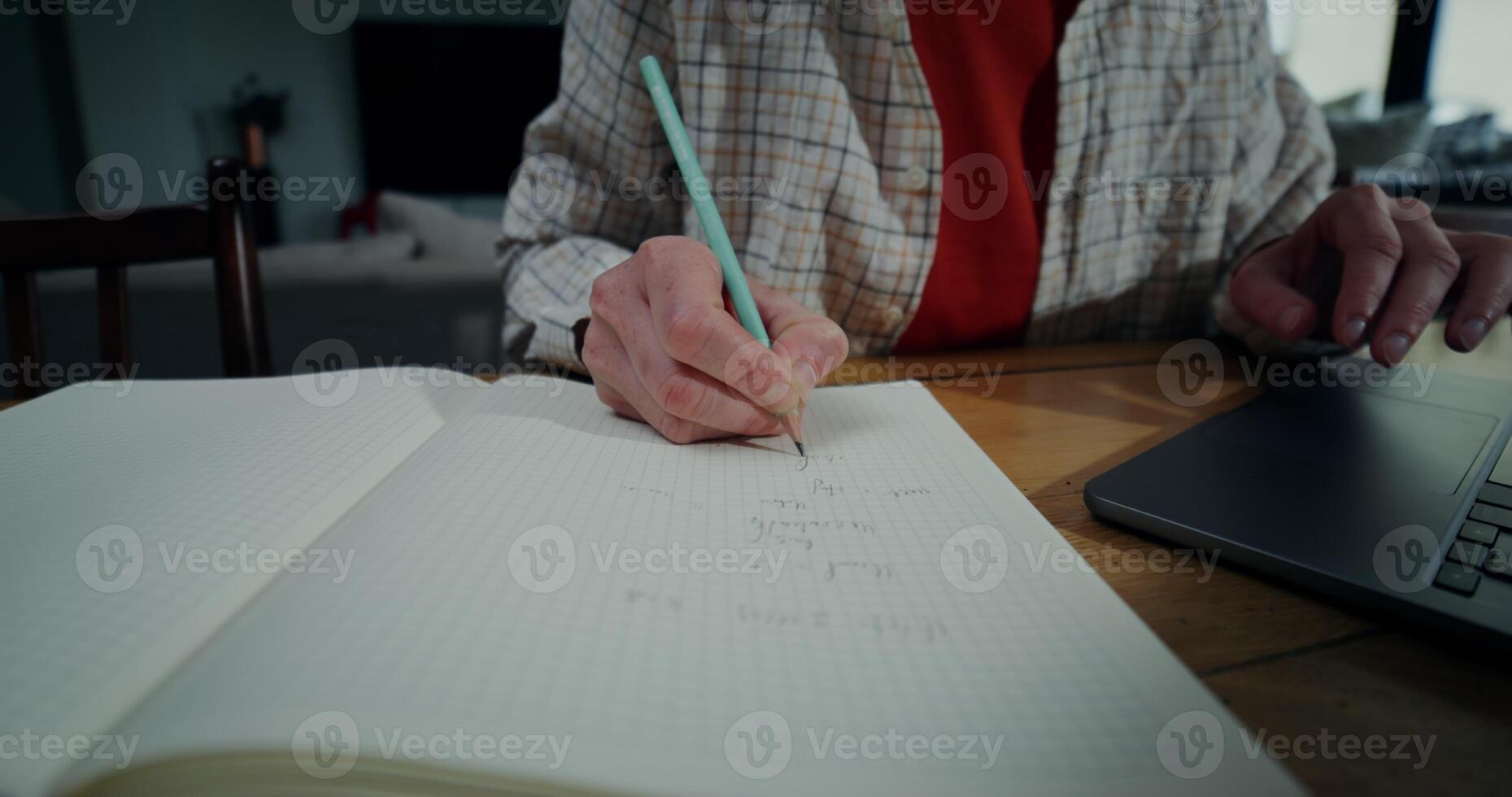 Woman in casual clothes writes in a notebook and uses a laptop while sitting at a table indoors, Close-up of women's hands, no face photo
