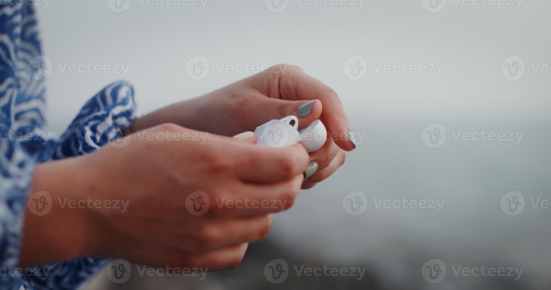 Close-up of female hands opening box of wireless headphones and taking out each earphone at a time. No face, unrecognizable person. On the seashore. 4k , red komodo photo