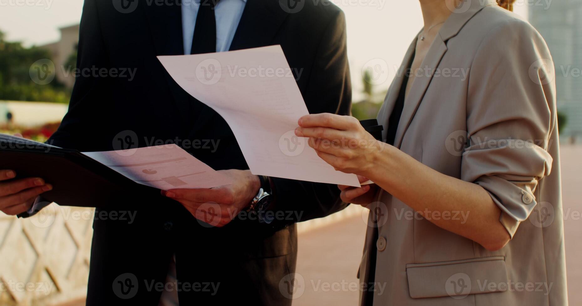 Man and a woman in business clothes are studying documents, talking with a serious look, standing on the street of a modern city photo