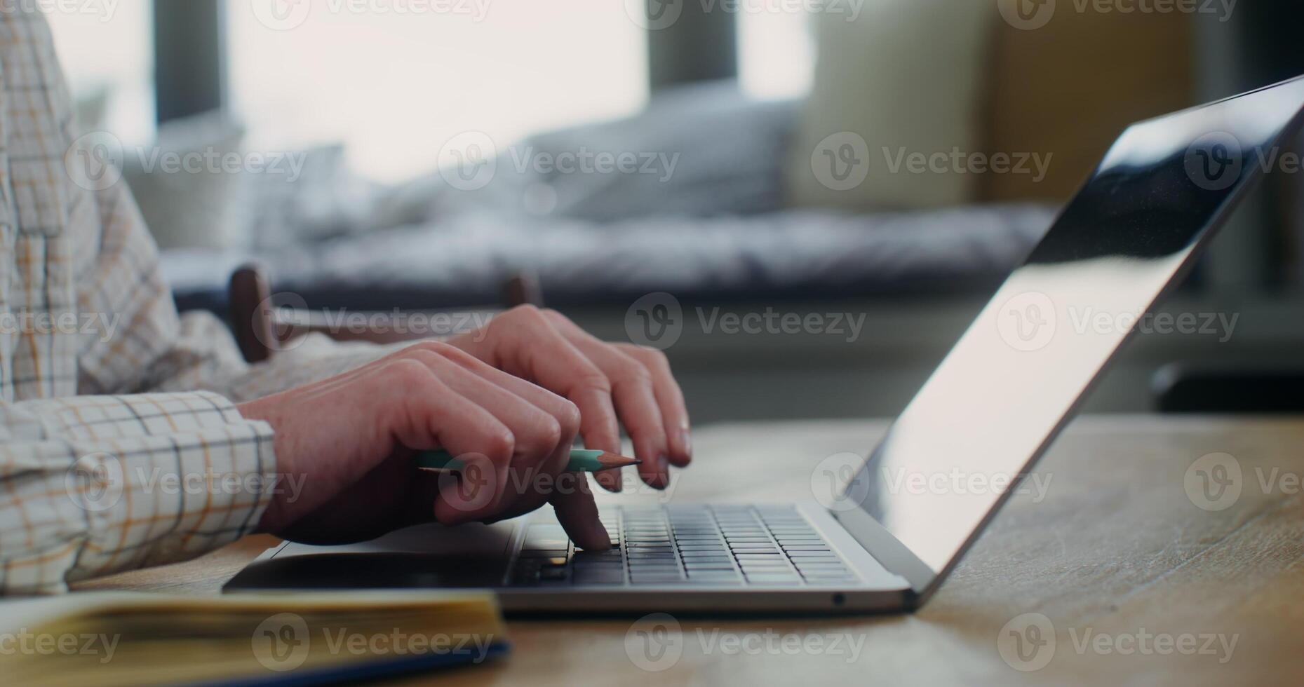 Woman in casual clothes is typing on a laptop keyboard while sitting at a table in a home interior, a close-up of a woman's hands, no face photo