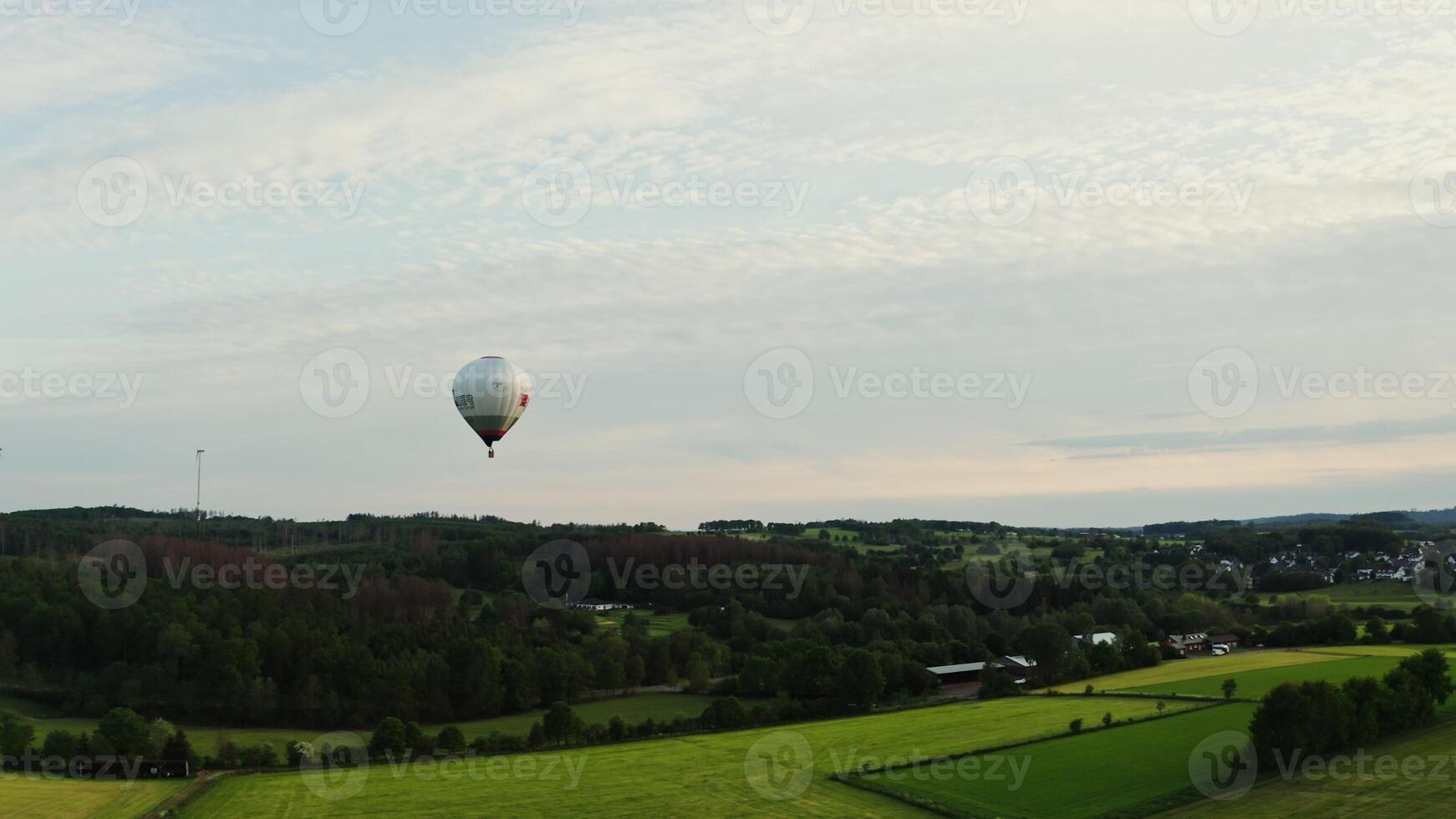 Drone shot of hot air balloon in the sky flying over a green valley near a village in Germany on a sunny day. photo