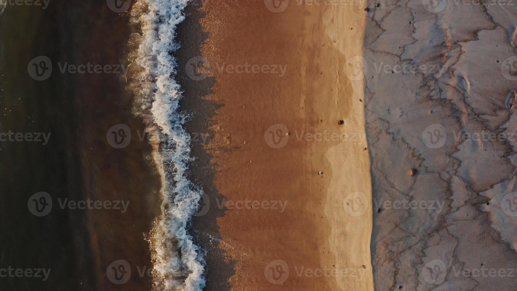 View of a sandy deserted beach washed by foamy sea waves. View from above, turning into a panoramic shot of the coastline. photo