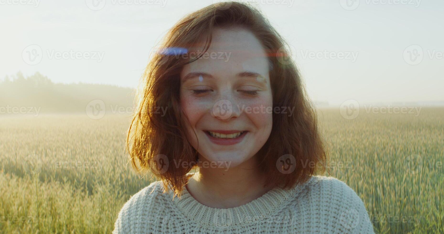 Rd-haired woman laughs while looking at the camera while walking through a wheat field in the bright light of the rising sun. Nice young face, close-up. 4k , red komodo photo