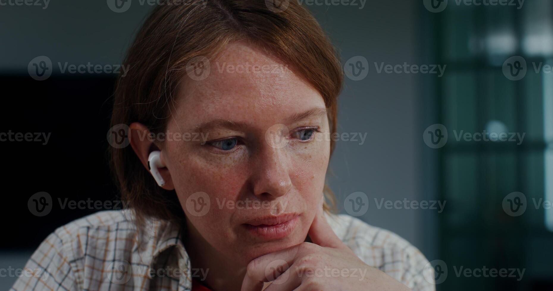 Blue-eyed red-haired woman with headphones in her ears smiles looking at the camera touching her chin with her hand photo