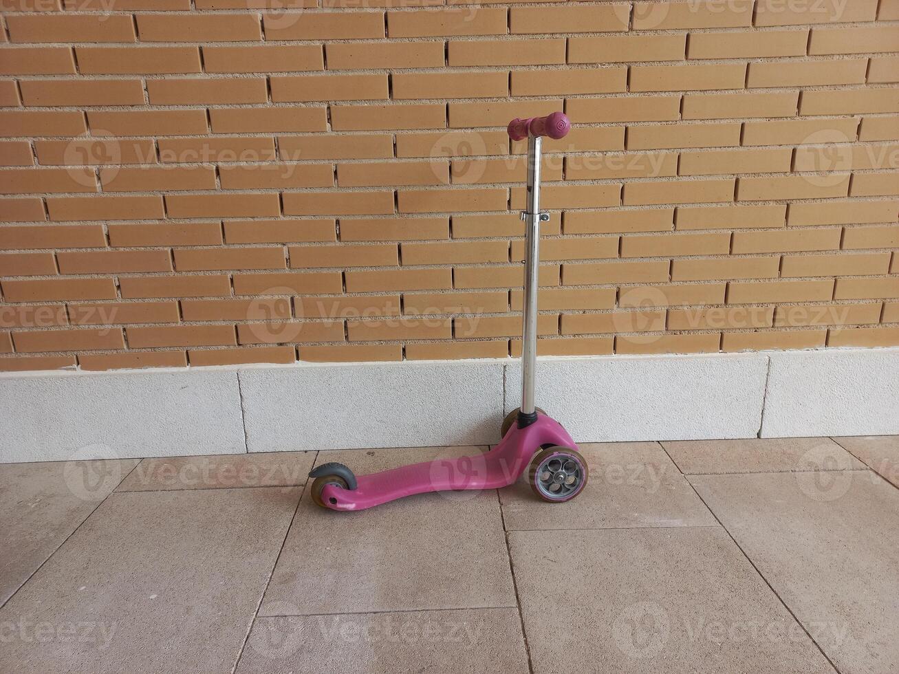 Bright pink scooter against brick wall for urban lifestyle or children's play concept photo