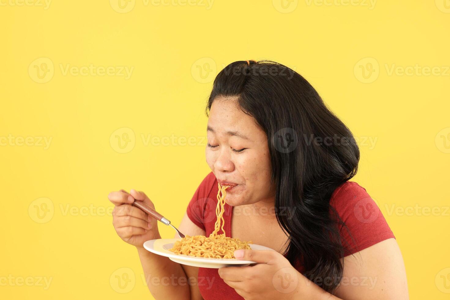 Big Fat Asian Woman in Red Shirt Eating Fried Noodles from Plate with Fork photo