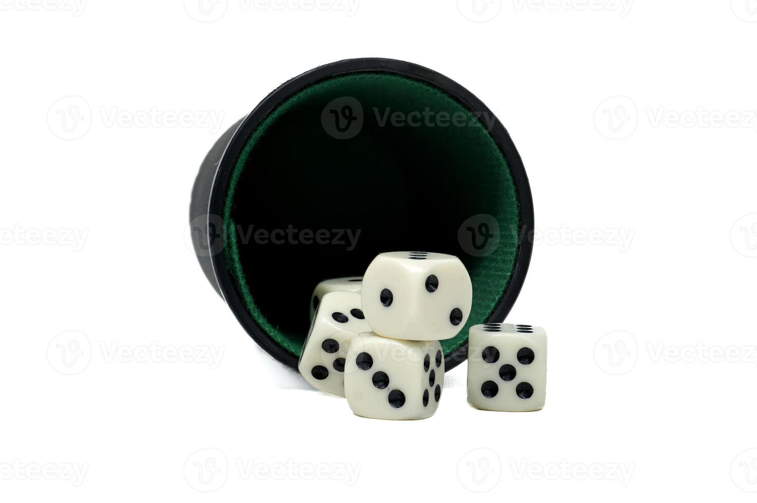 A dice cup has spilled, scattering several white dice with black spots across a white surface. photo