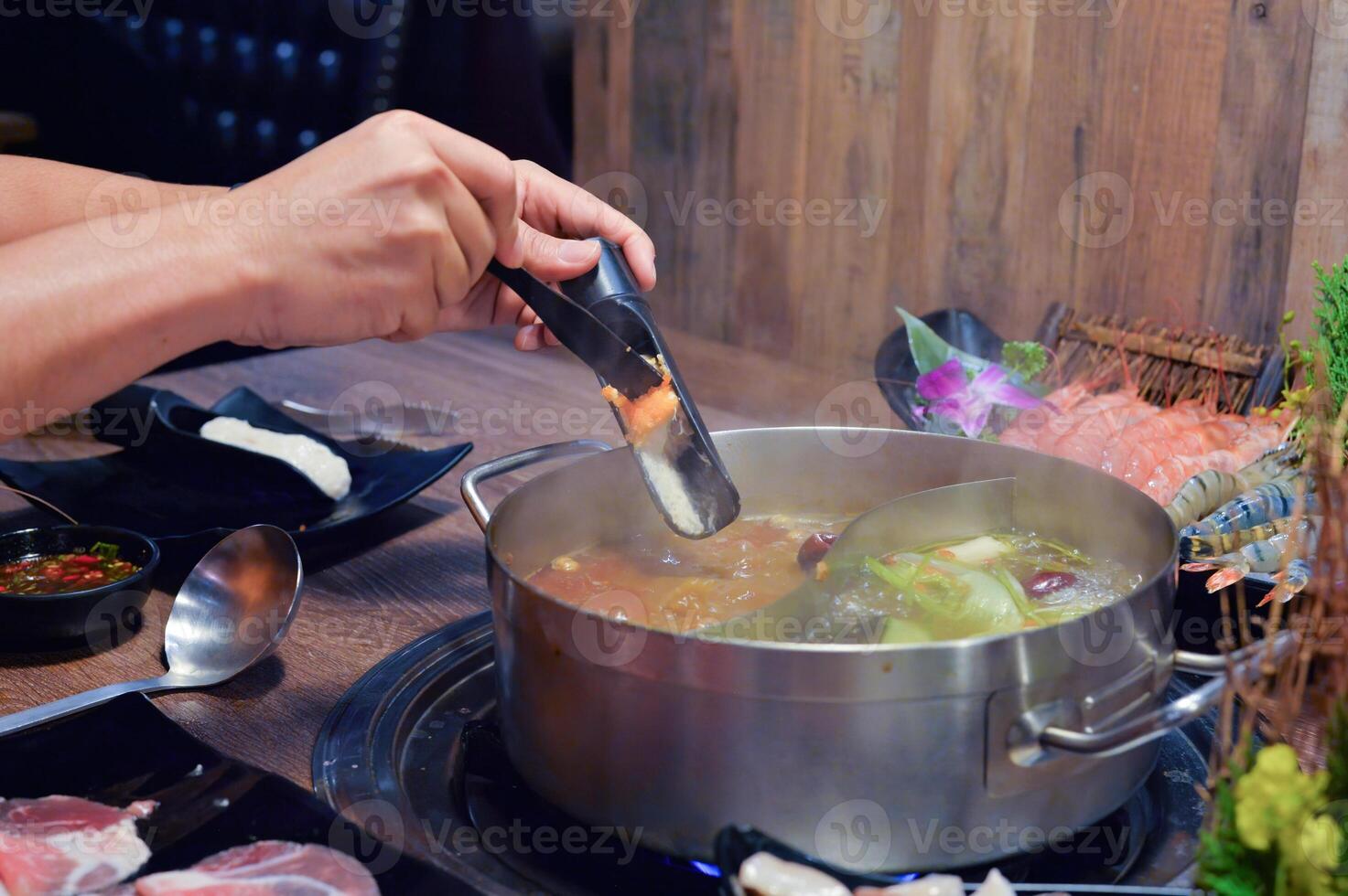 Hand Adding Ingredient to Boiling Hot Pot Meal photo