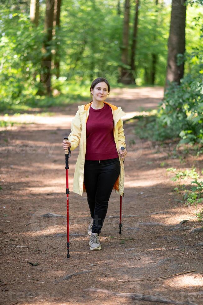 A woman with a yellow jacket and black pants is walking on a trail photo