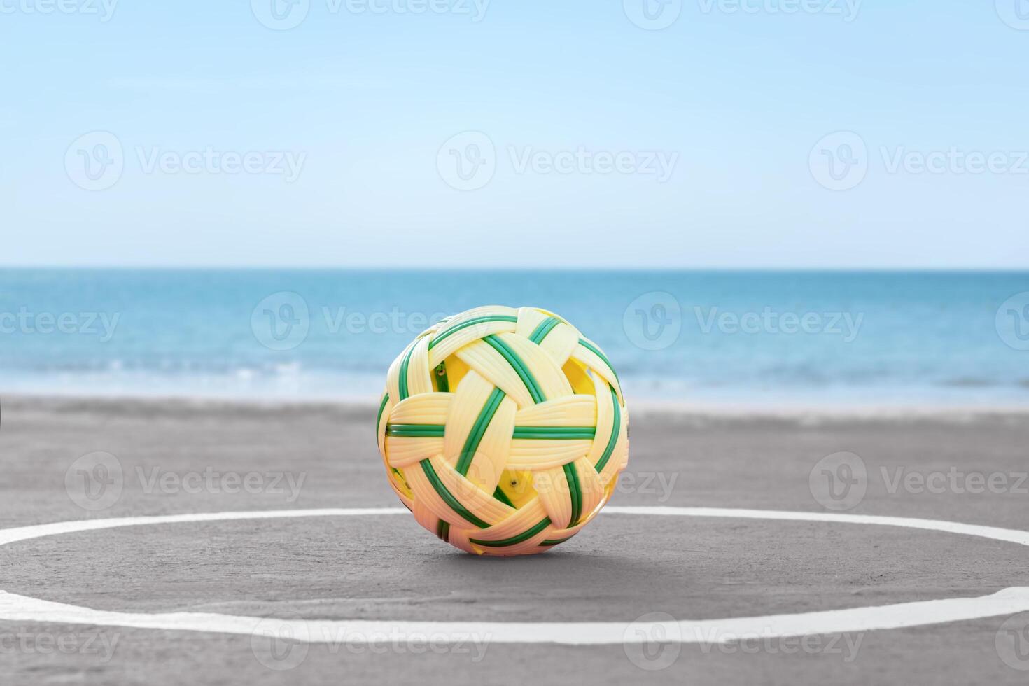 A traditional woven sepak takraw ball on a seaside court, with the calm ocean and blue sky in the background. Perfect for sports, culture, or beach lifestyle themes. photo