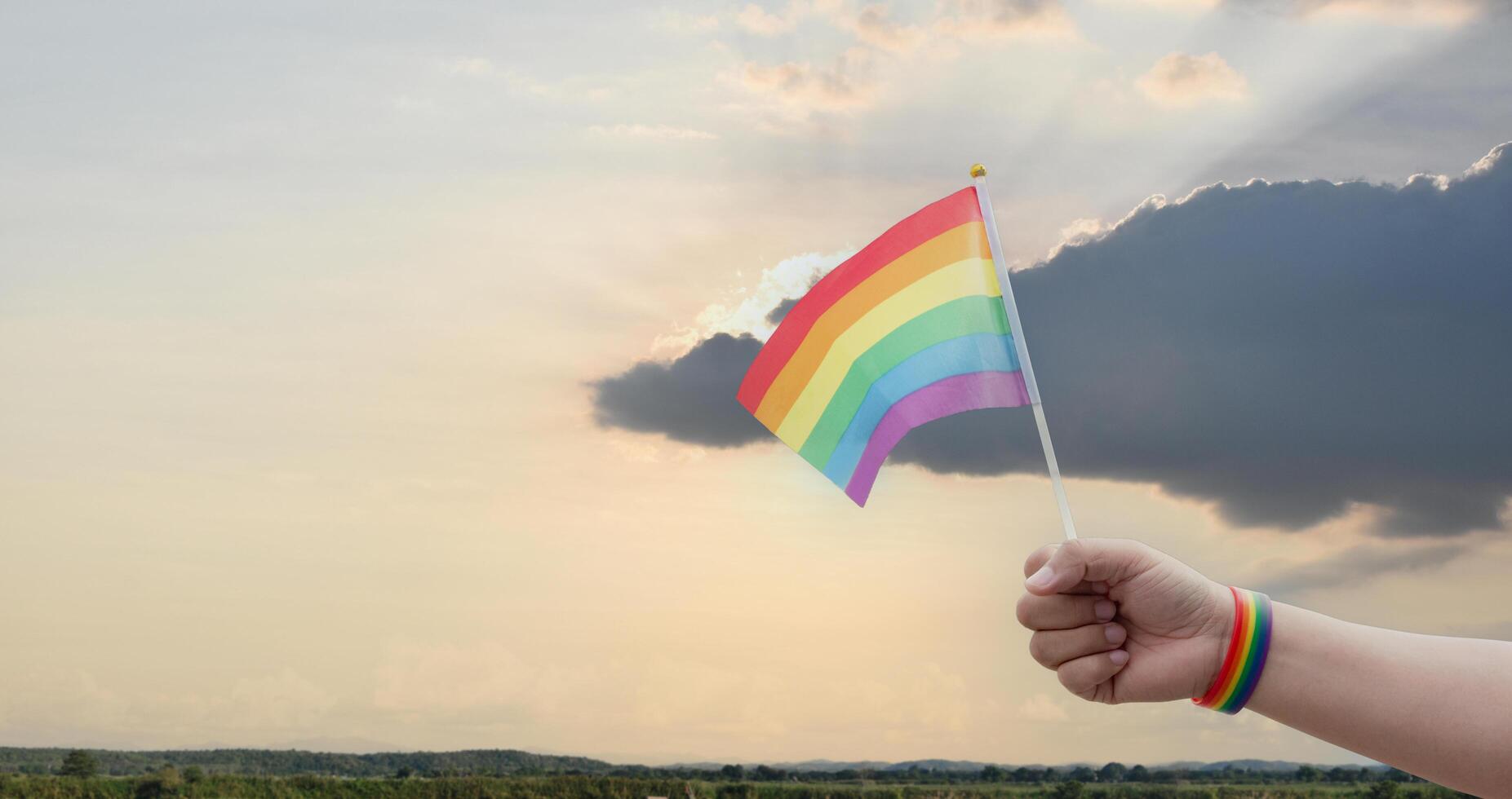 Rainbow flags showing in hands against clear bluesky, copy space, concept for calling all people to support and respcet the genger diversity, human rights and to celebrate lgbtq in pride month. photo