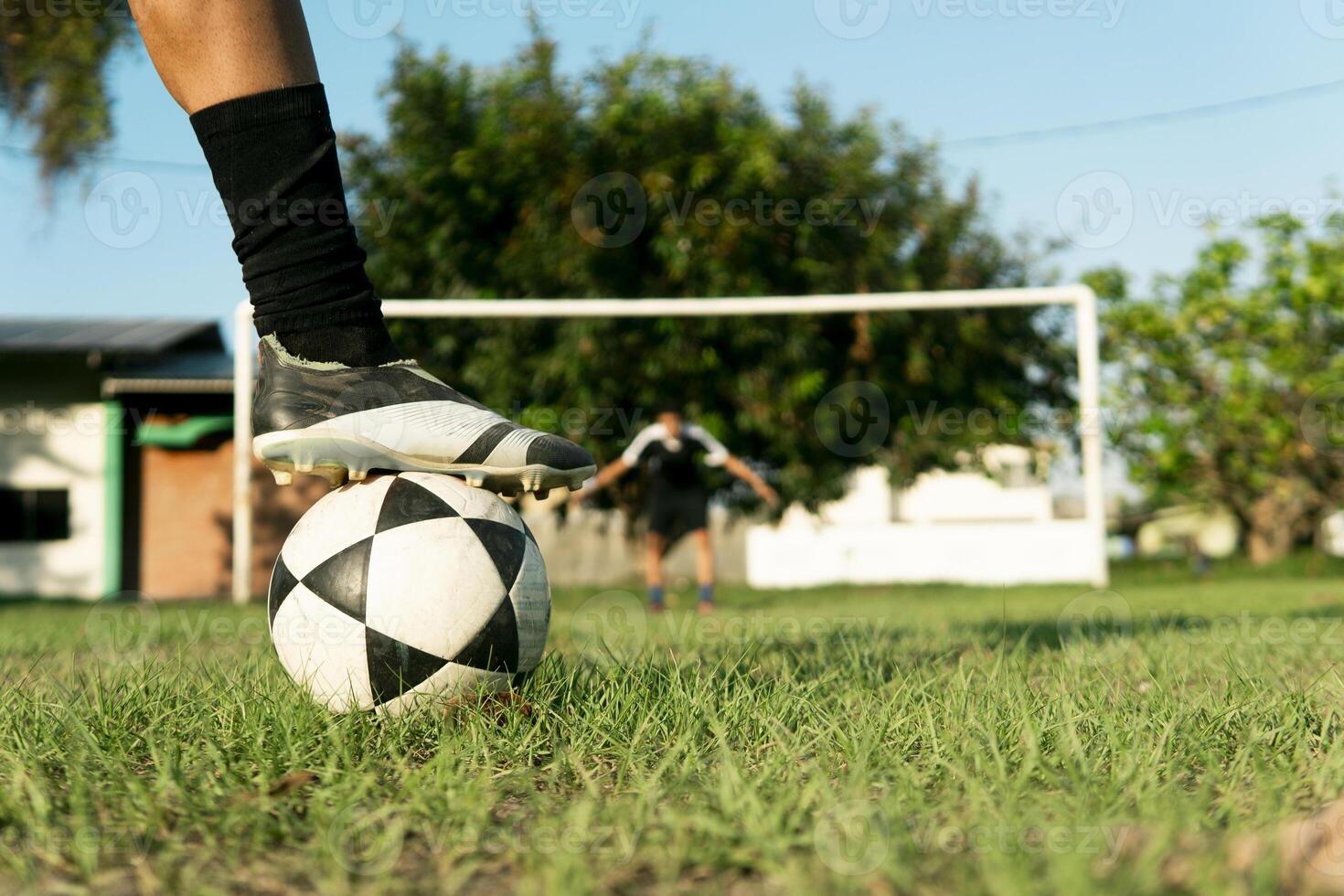 Soccer player placing their cleat on top of ball with goalkeeper in background photo