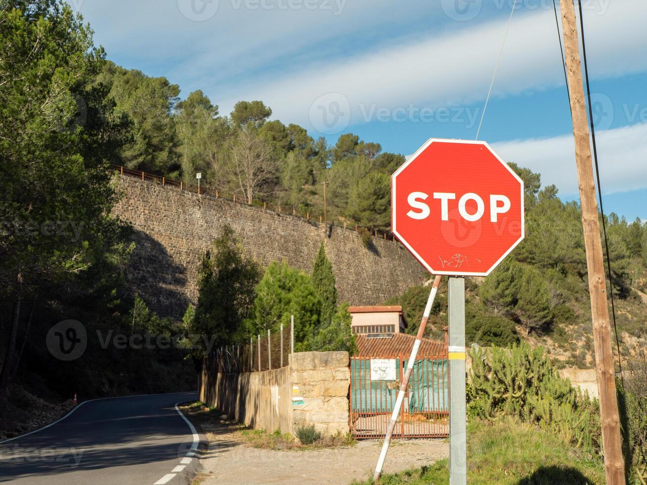 Red stop sign placed on sharp road turn near rustic stone wall in mountainous area on bright sunny day. Ideal for travel blogs, safety concepts and transportation visuals photo