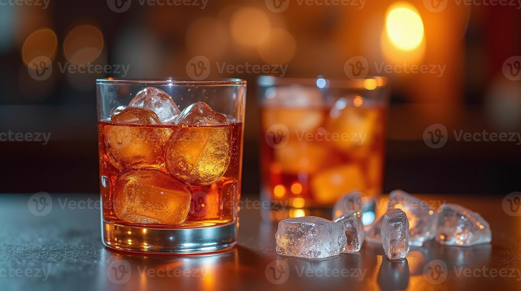 Two crystal glasses filled with amber liquid and ice cubes on a dark surface. photo