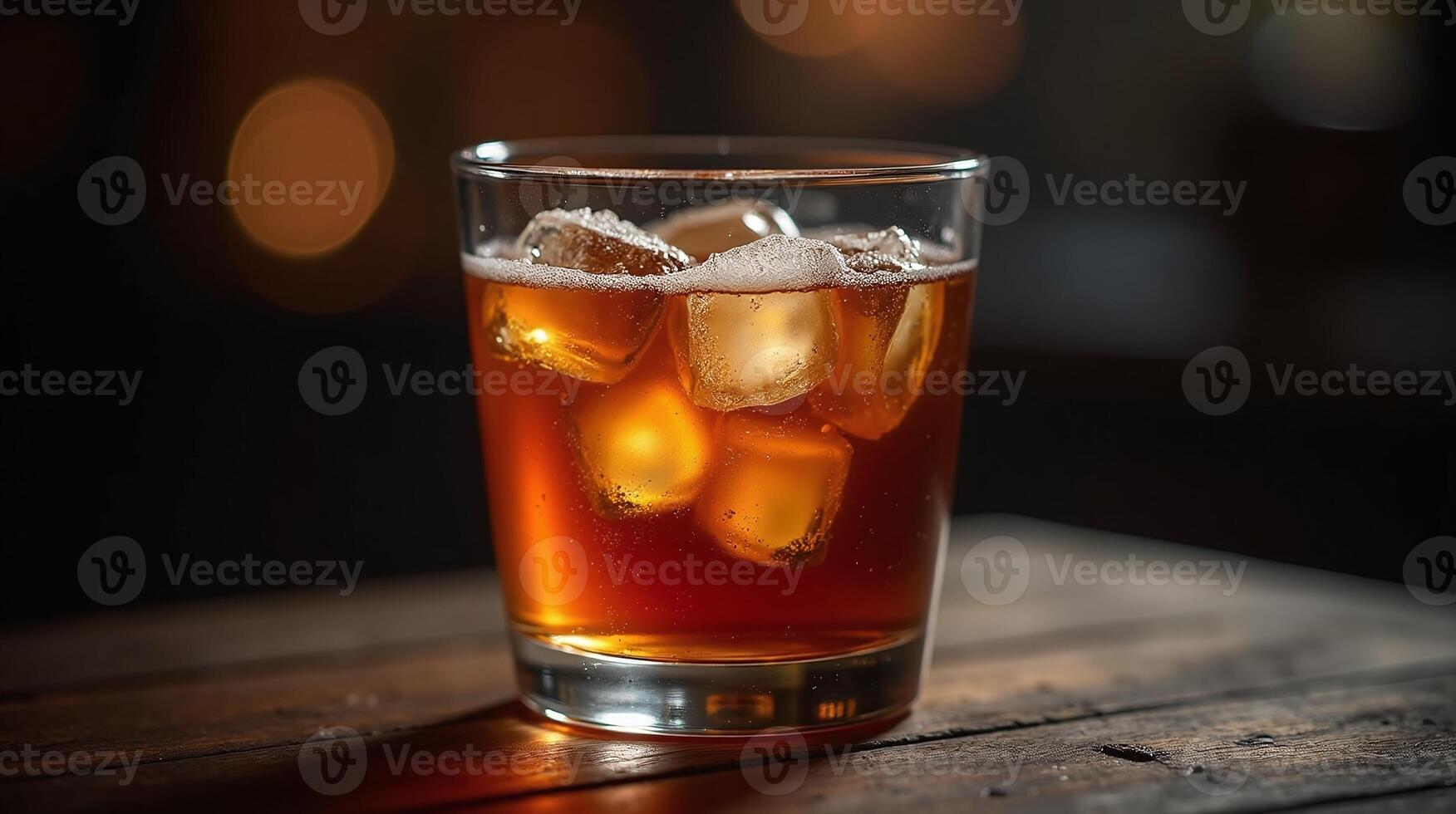 A glass of amber-colored beverage with ice cubes on a wooden surface against a blurred backdrop. photo