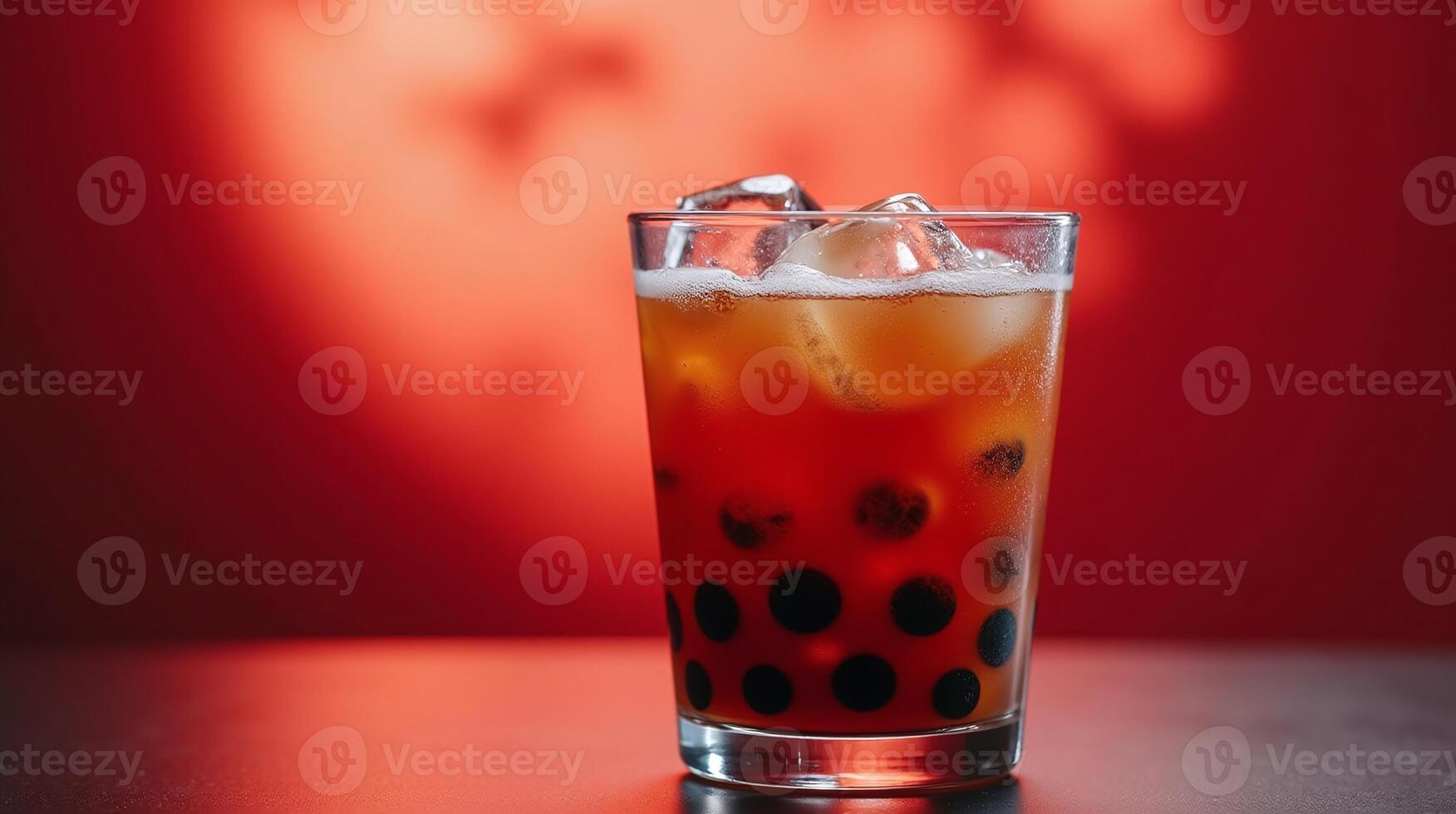 A clear glass with ice and a dark liquid in the foreground against a red background. photo