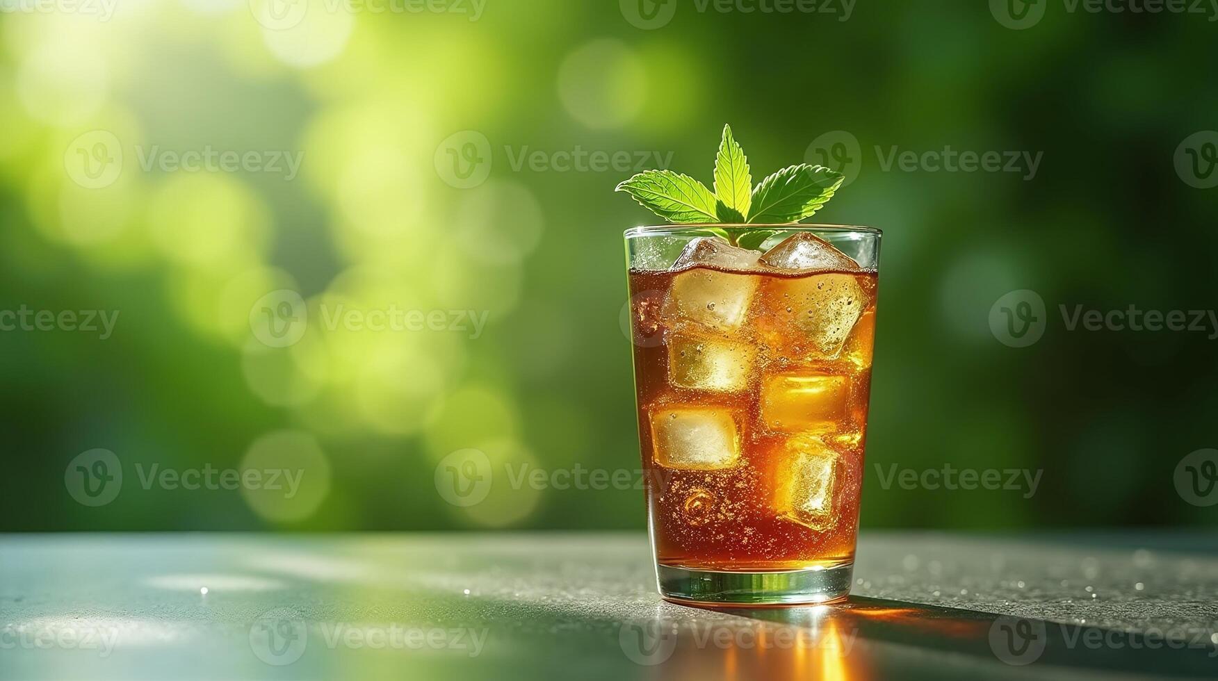 A glass of iced tea with ice cubes and a mint sprig, placed on a surface against a blurred green background. photo