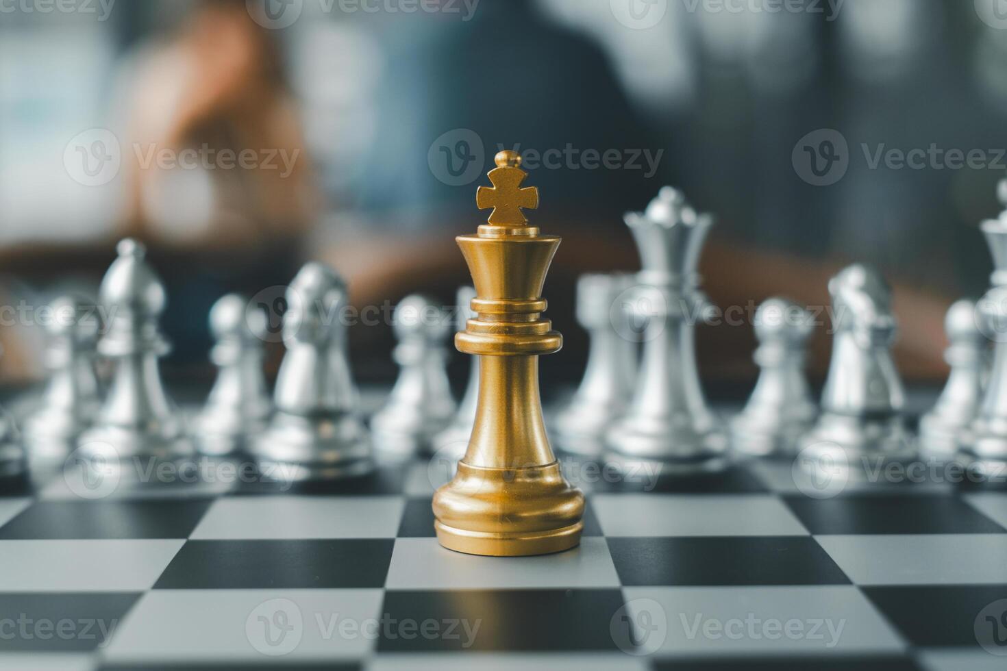 A golden chess king stands prominently on a chessboard surrounded by silver pieces, symbolizing strategy and leadership. photo