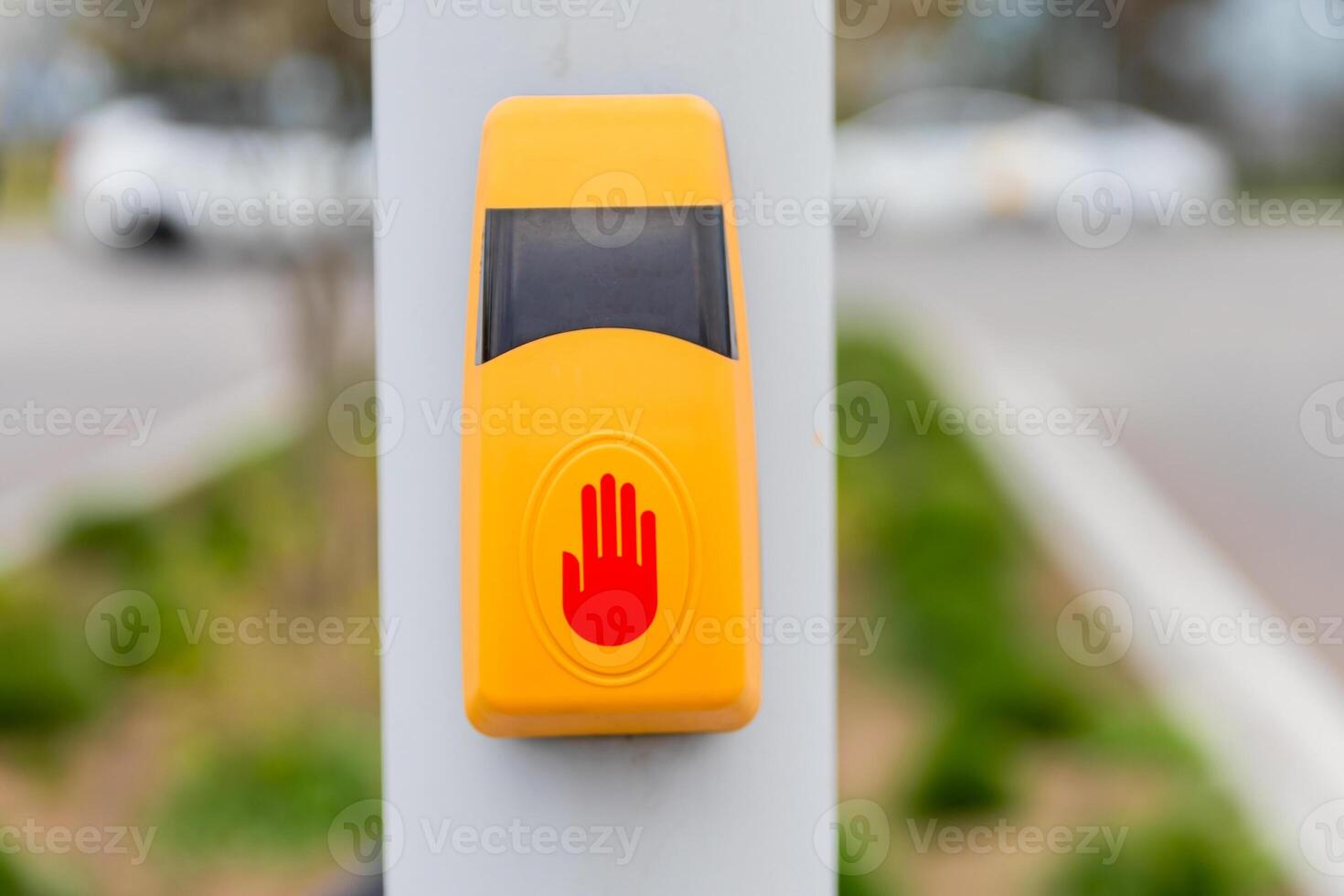Yellow pedestrian crossing button with a red hand symbol mounted on a pole beside a street. photo