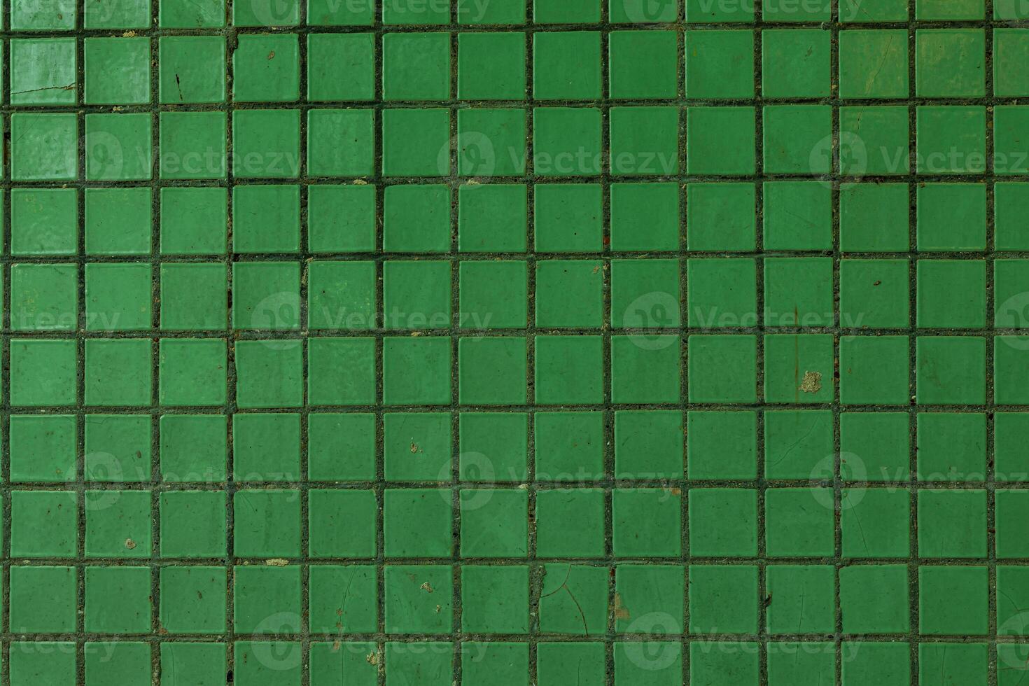 Close-up of a green ceramic tiled wall with visible grout lines and minor surface imperfections, ideal for backgrounds or design elements. photo