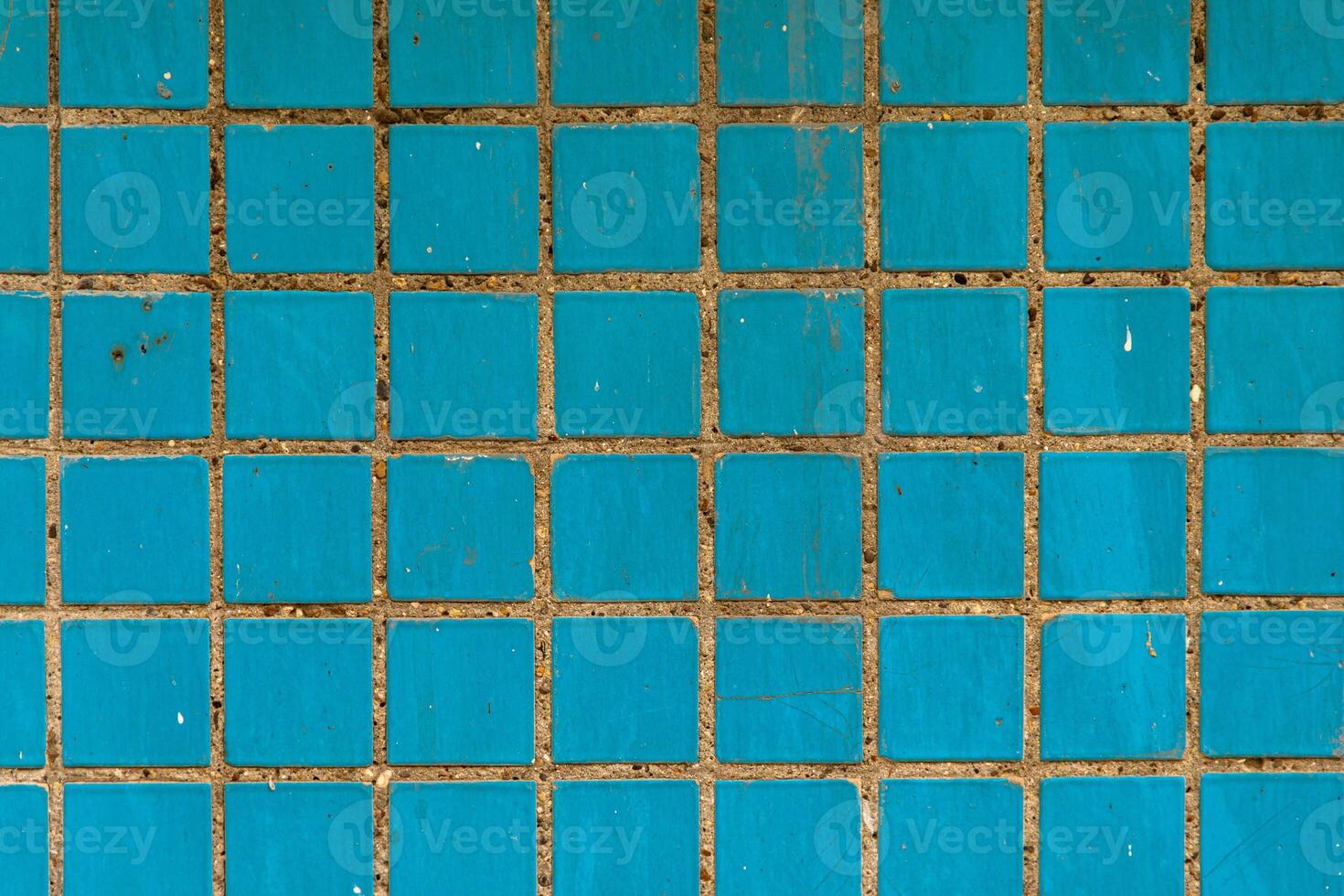 Square blue ceramic tiles with worn grout and surface scratches, creating a gritty, urban wall texture for design and architectural backgrounds. photo