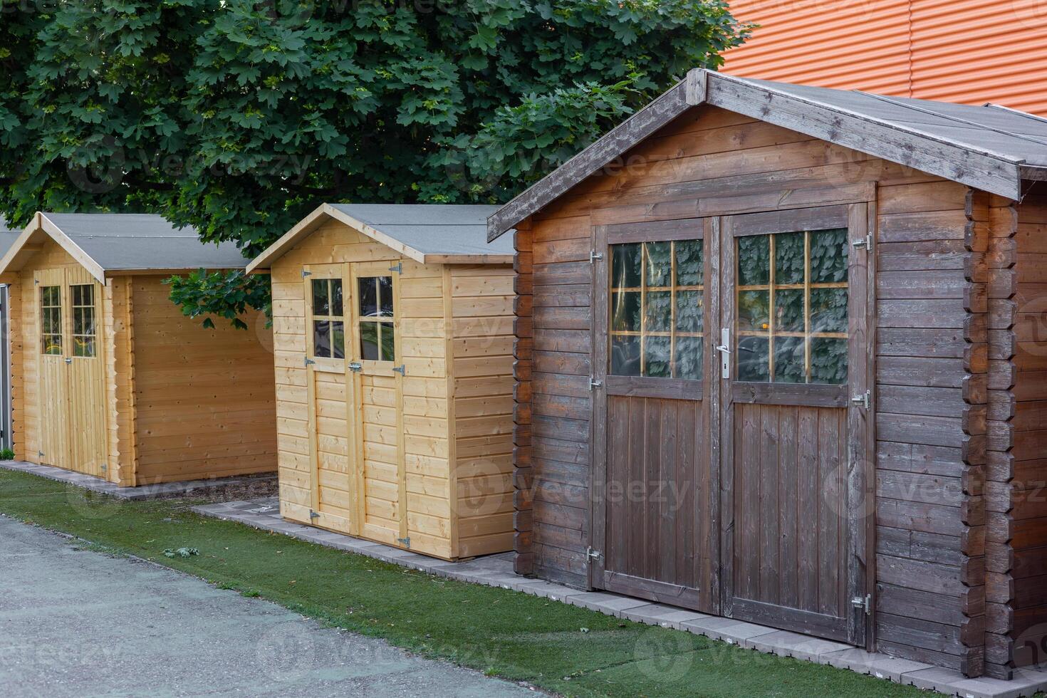 Wooden garden sheds displayed on artificial grass with tree in background photo