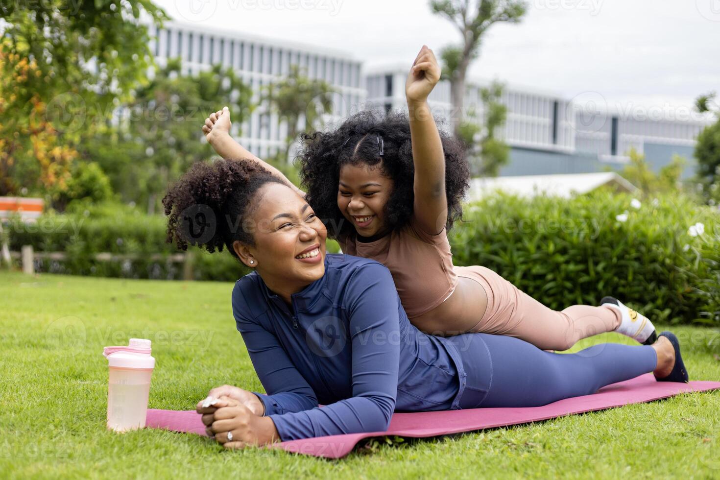 African American mother and young daughter are lying down and playing ride after having yoga exercise public park for weekend leisure and happiness photo