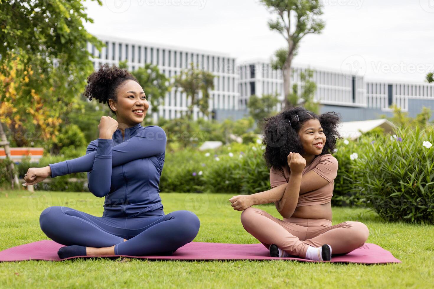 African American woman and daughter in yoga suit are relaxingly practicing healthy stretching exercise together in the park for stiff muscle and preventing office syndrome photo