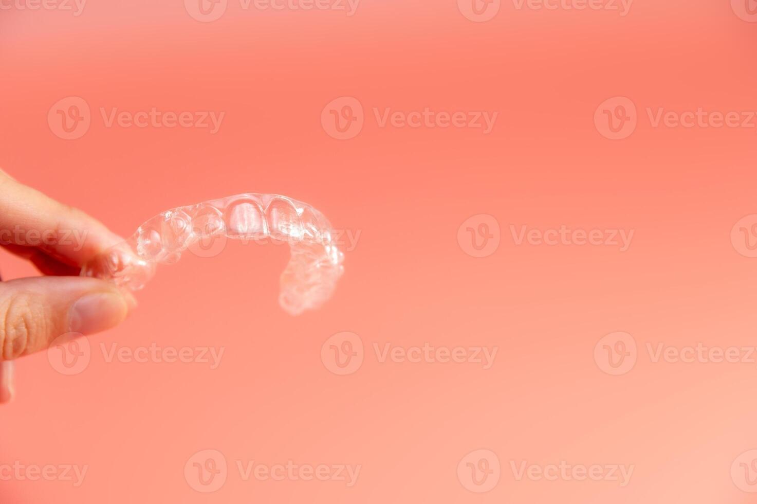 Hand holding plastic braces on pink background. Female hand showing modern methods of teeth straightening photo
