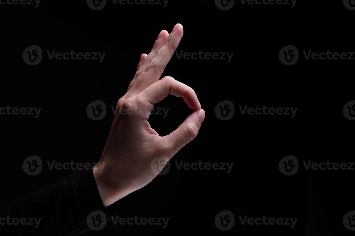 Female hand showing the ok gesture on a black background. Okey hand sign photo