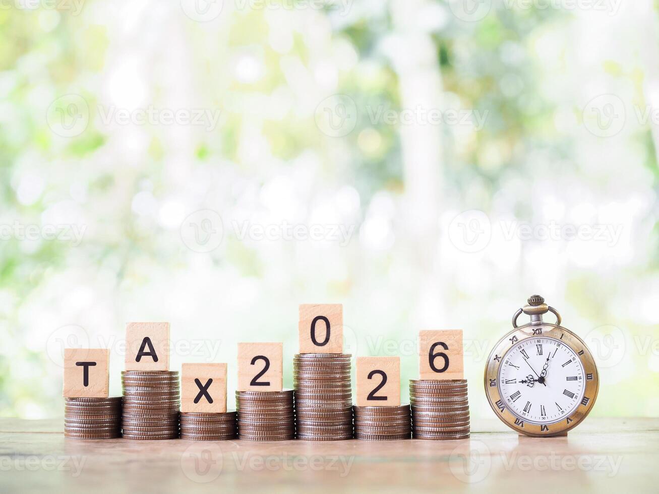 Vintage watch, Wooden blocks with the word TAX, Nunber 2025 and stack of coins. The concept about saving money and manage time to paying tax in year 2026 photo