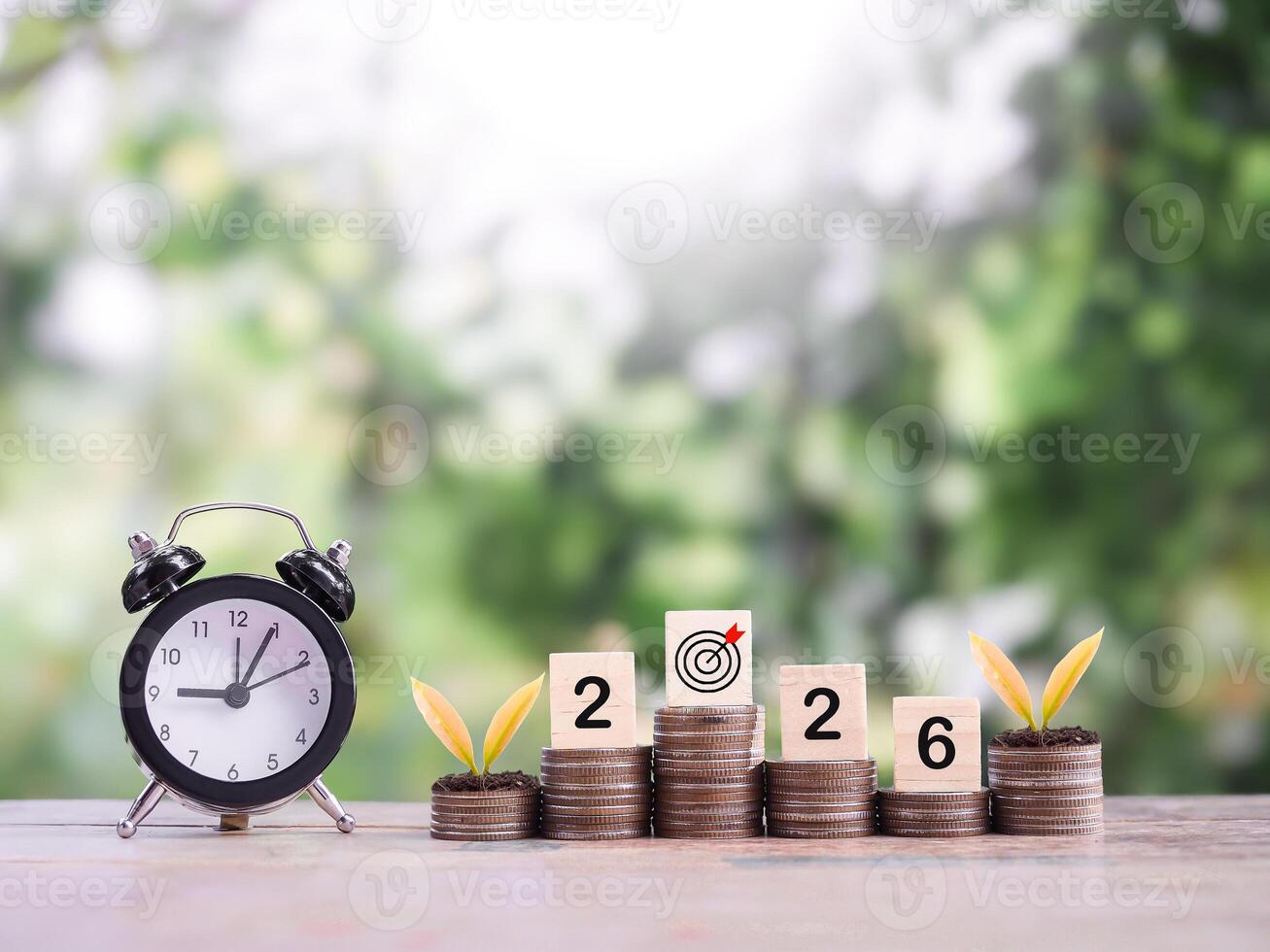 Black alarm clock, Wooden blocks with the number 2026 and plants growing up on stack of coins. The concept of saving money for manage time to success business in year 2026 photo