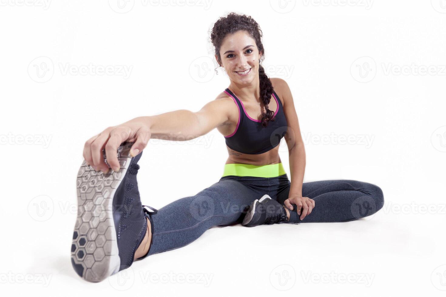 beautiful smiling athlete in sportswear doing leg exercises sitting isolated on white background photo