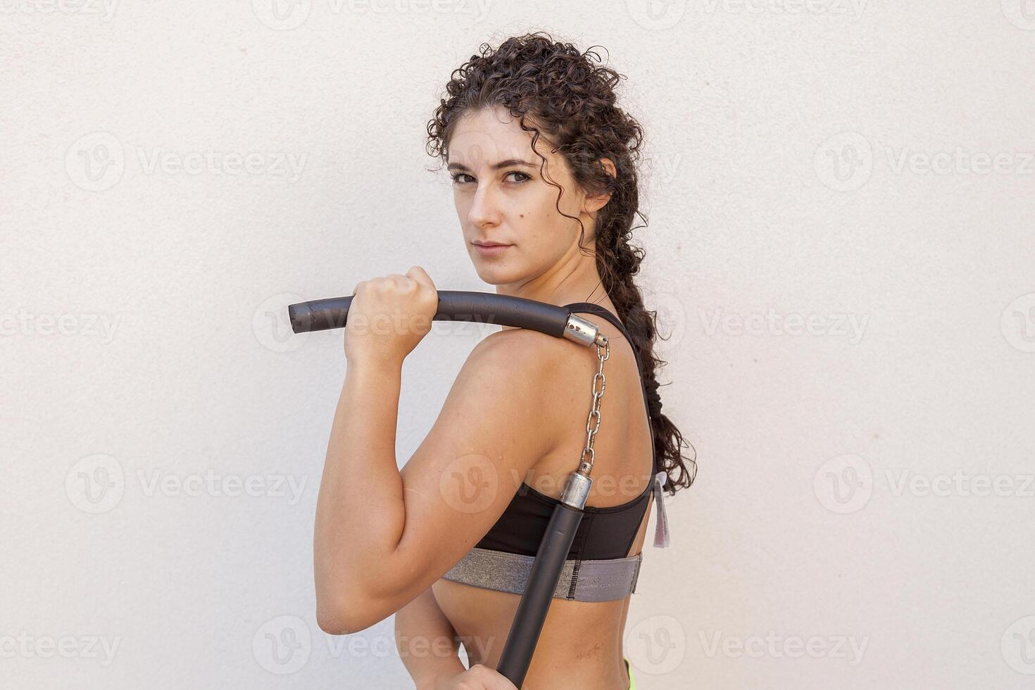 portrait of beautiful female athlete showing nunchaku weapon outdoors photo