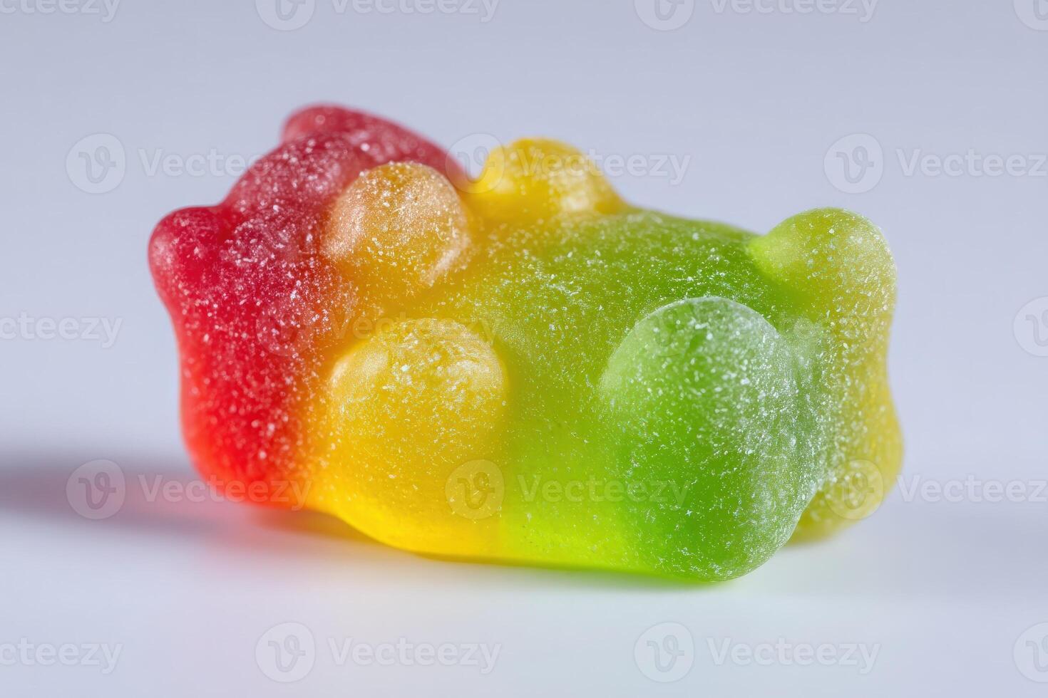 A vibrant gummy bear candy lies on its back, showcasing a rainbow of colors including red, yellow, and green. Its sugary texture glistens under soft light, making it an appealing treat. photo
